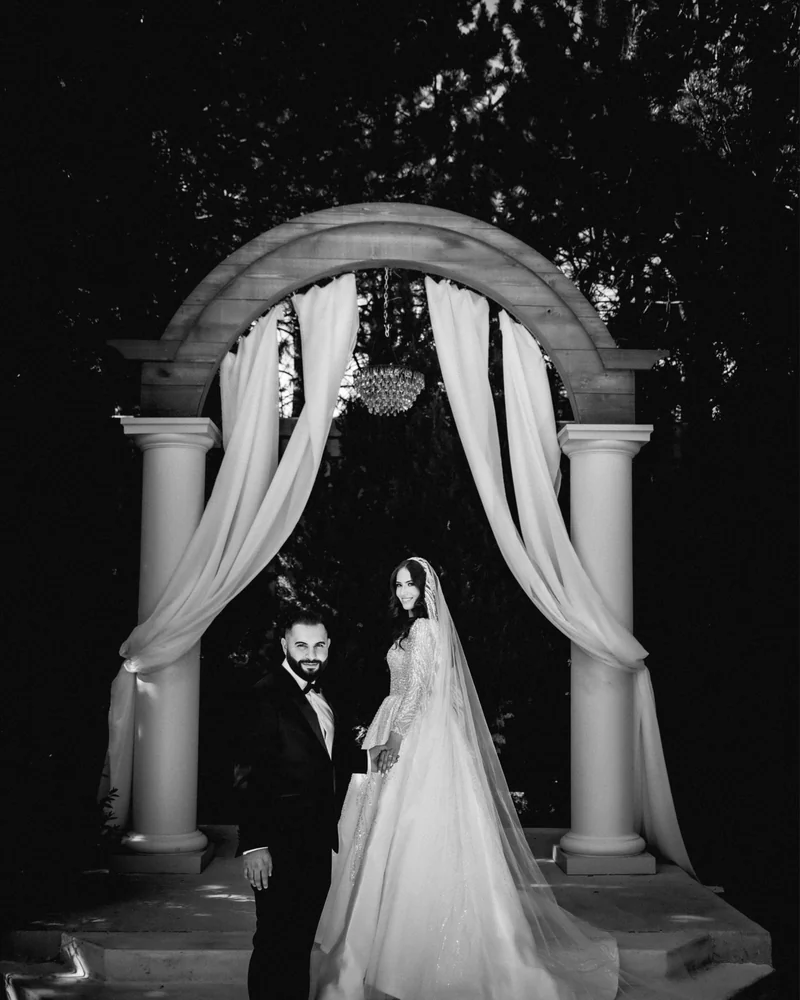 Black and white portrait of a couple beneath a draped ceremony arch